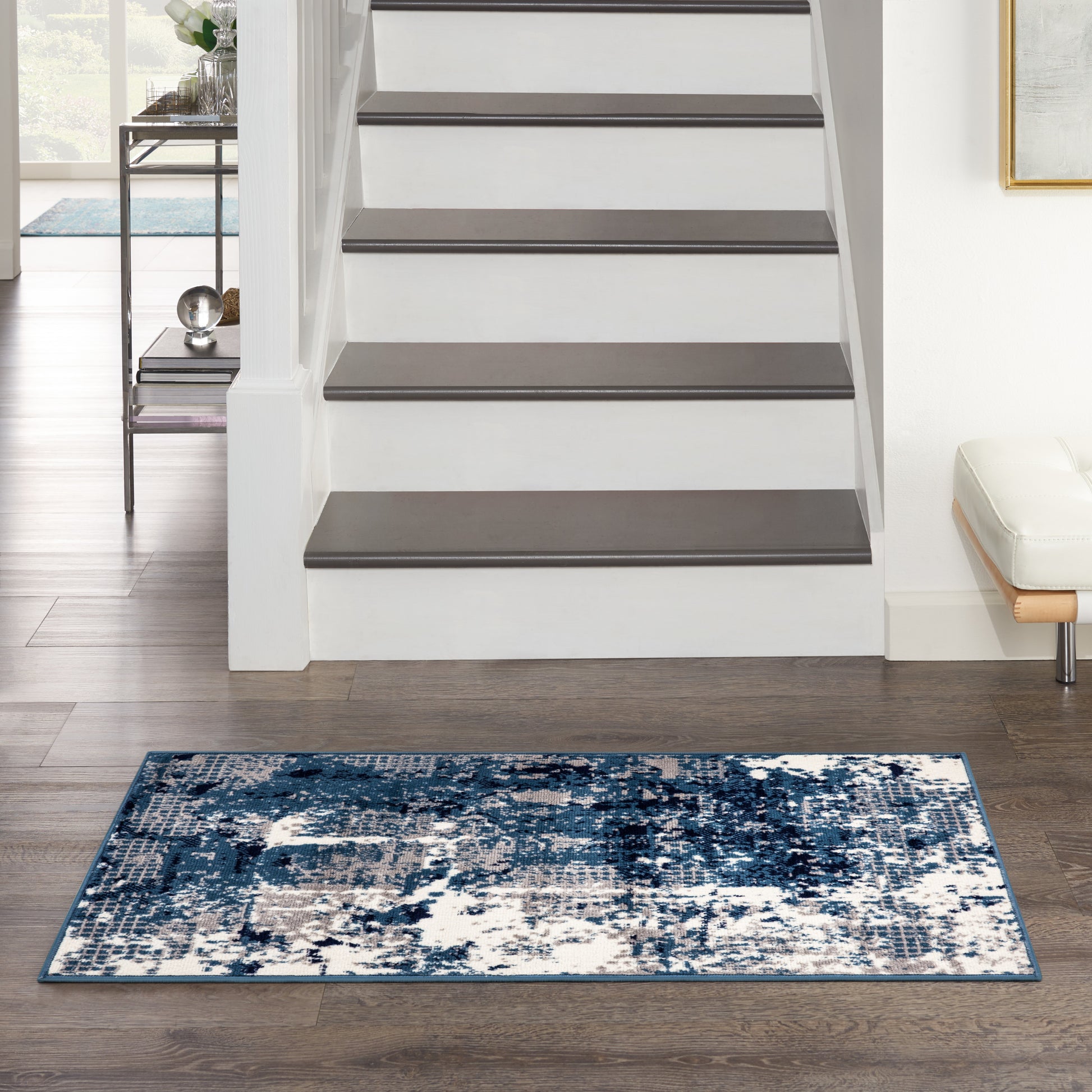 Abstract blue and white area rug on dark wood floor in front of a white staircase, modern living area.