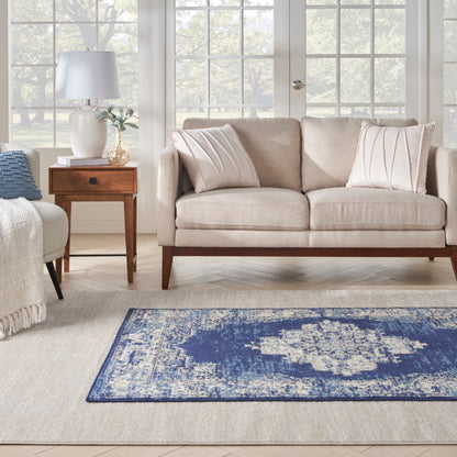 Blue distressed rug 5' x 7' on beige carpet in a living room; beige sofa with wooden legs and a wooden side table visible.