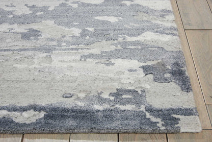 Abstract blue-gray and ivory rug with cloud-like pattern on wooden floor, soft pile.