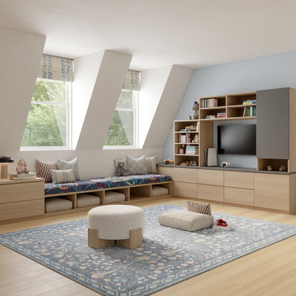 Bright kids' room with light wood built-in storage, cushioned bench, blue patterned rug, ottoman and wall shelves with TV.
