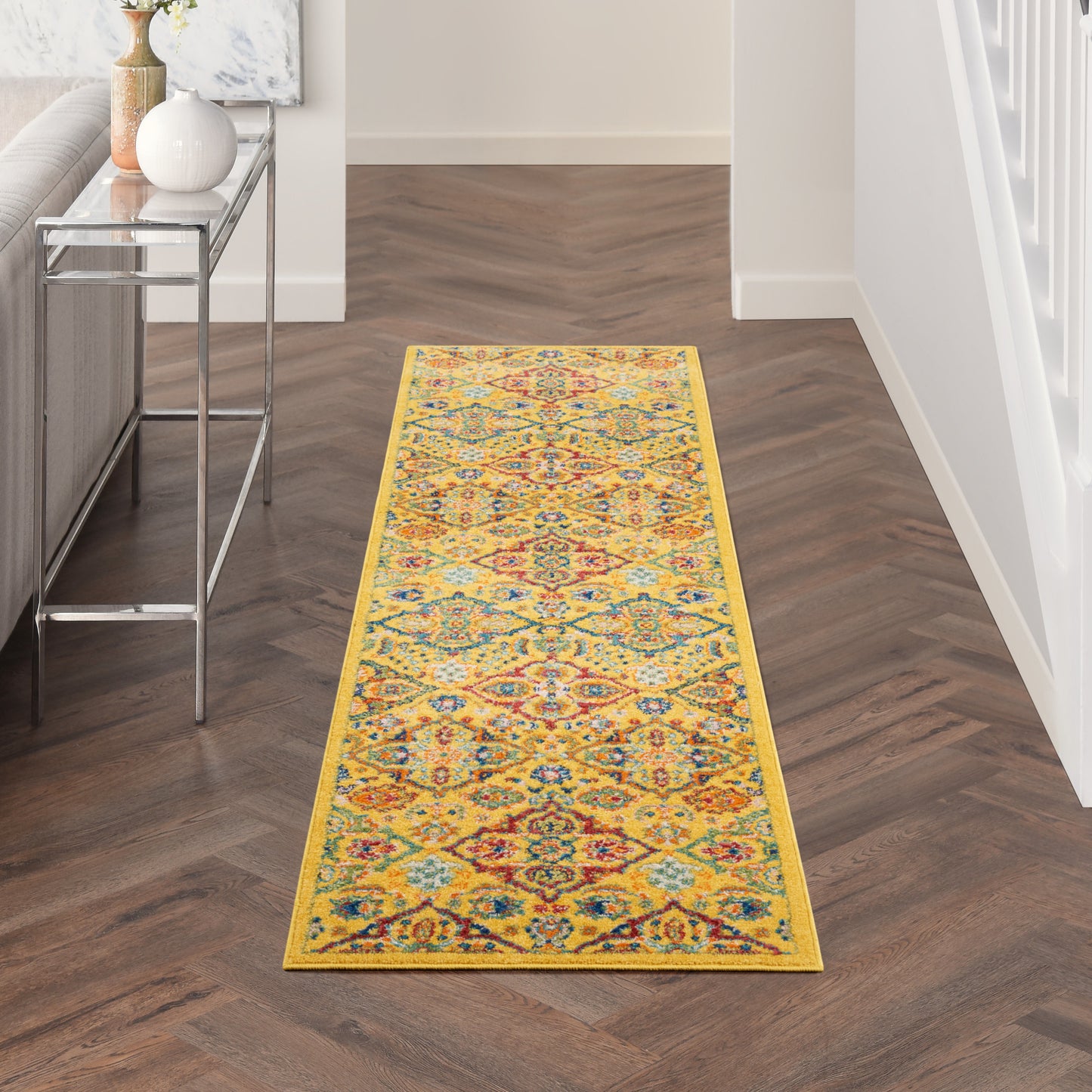 Long yellow oriental-style runner rug with multicolored geometric medallions on a dark wood hallway floor.