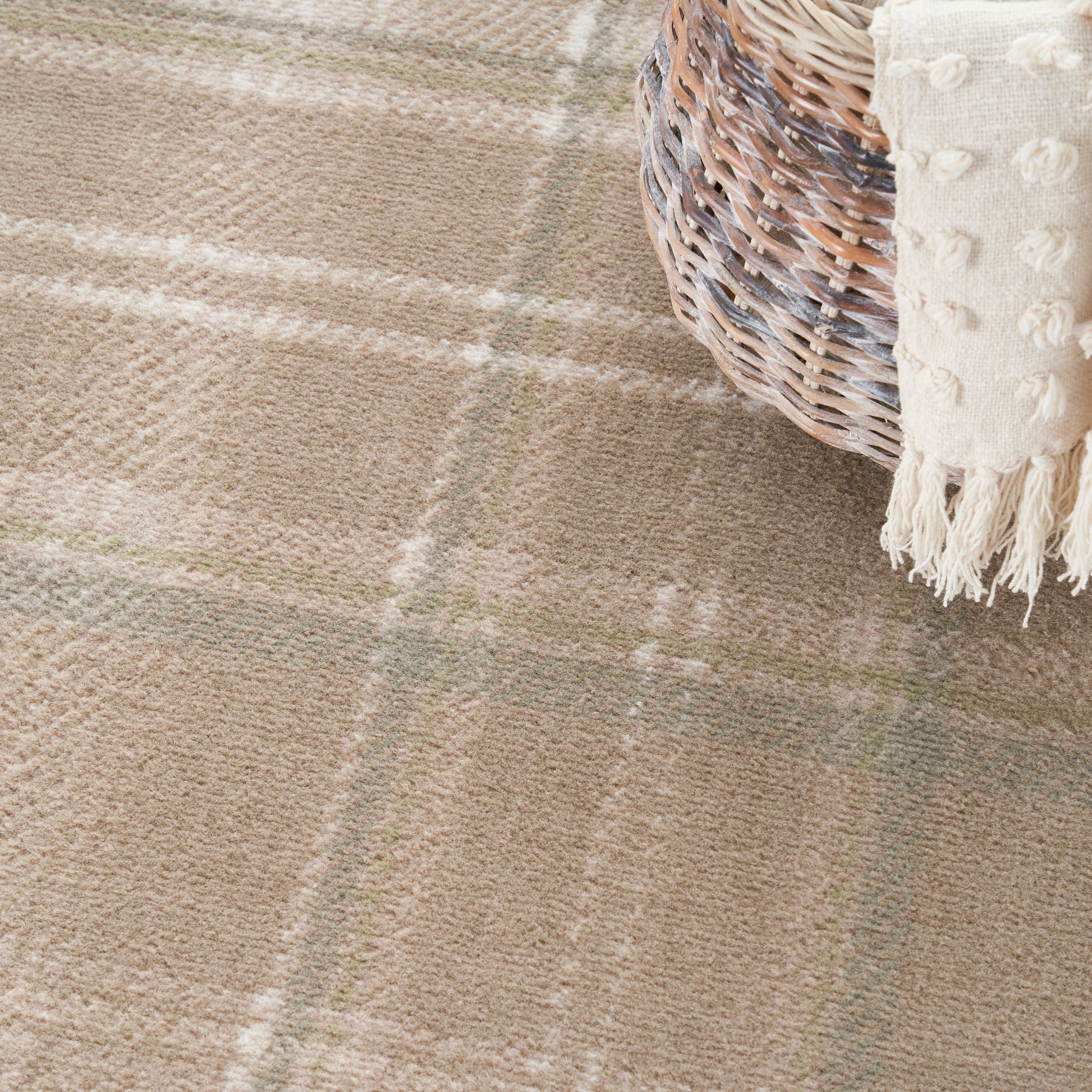 Beige plaid rug with soft texture and pale green lines, woven basket with cream fringed throw draped over edge.