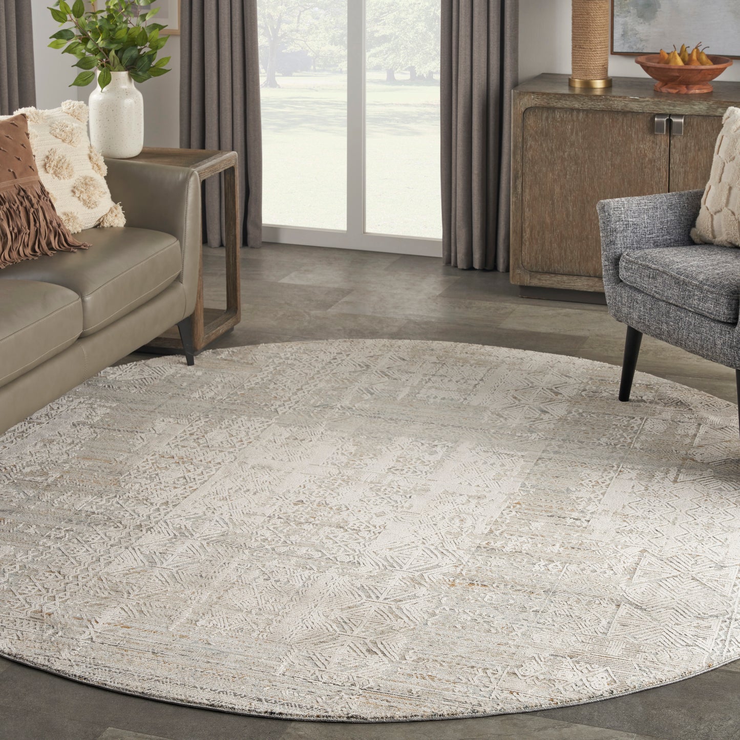 Round beige geometric patterned area rug in a contemporary living room with taupe sofa, gray armchair, and wooden sideboard.