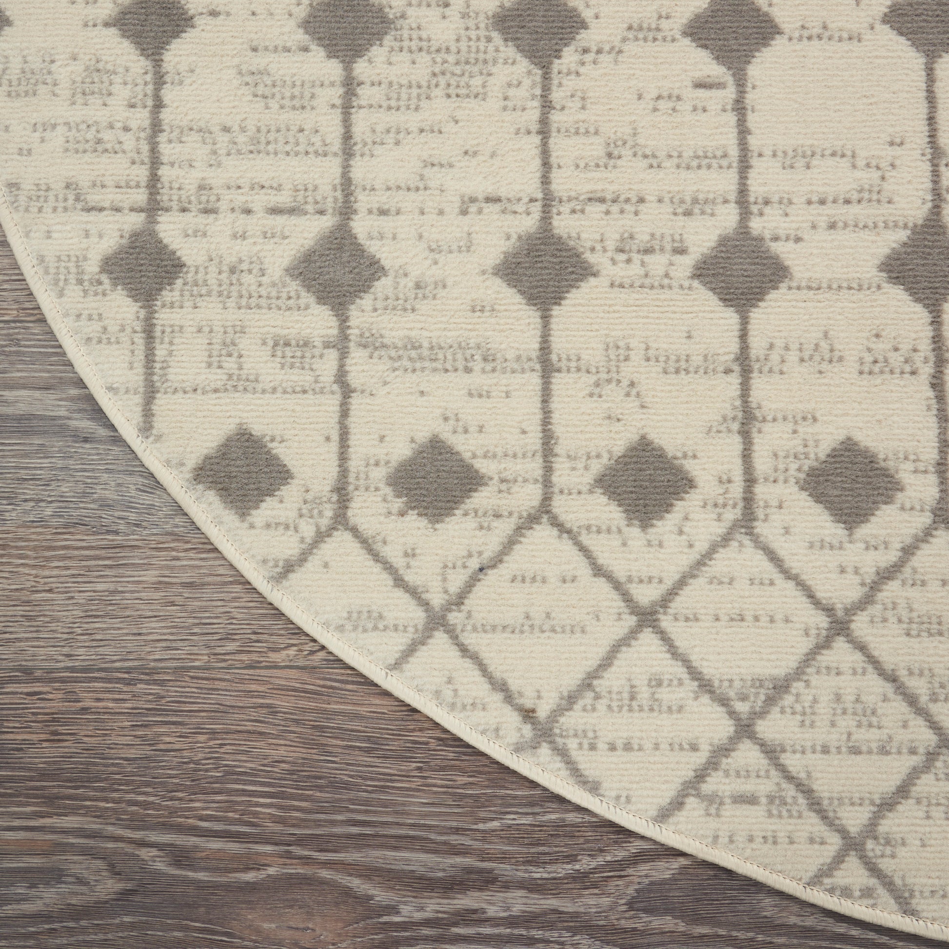 Beige and taupe geometric lattice rug with diamond motif on wood floor; curved edge visible.