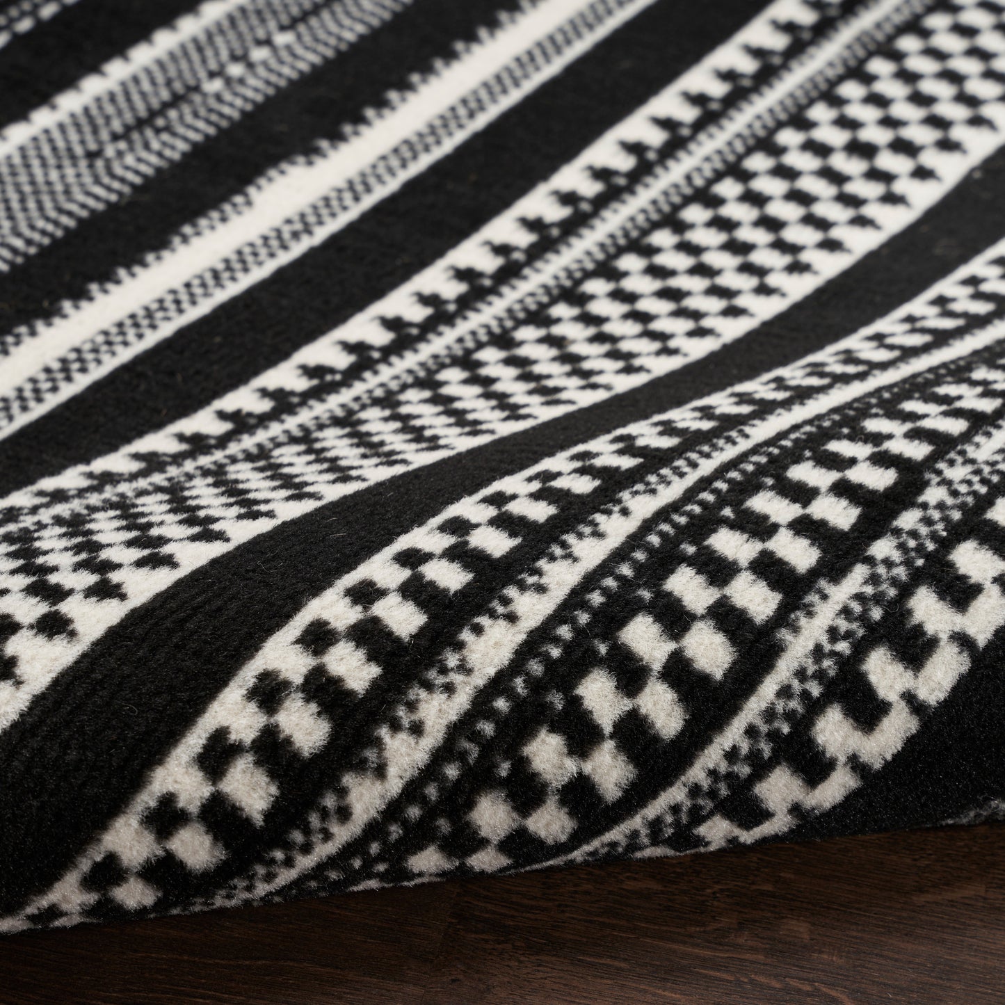 Black and white geometric woven rug with striped tribal patterns on dark wood surface.