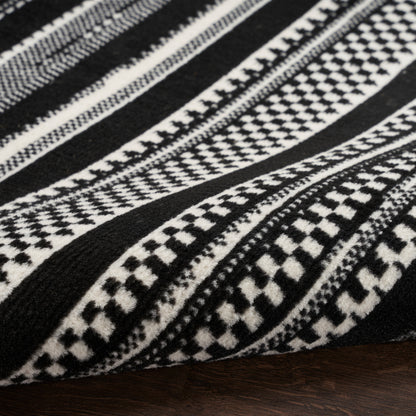 Black and white geometric woven rug with striped tribal patterns on dark wood surface.