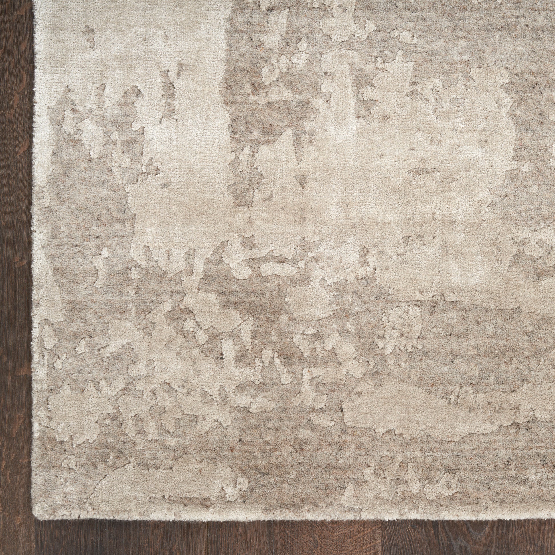 Soft beige distressed area rug with mottled taupe pattern on dark hardwood floor.