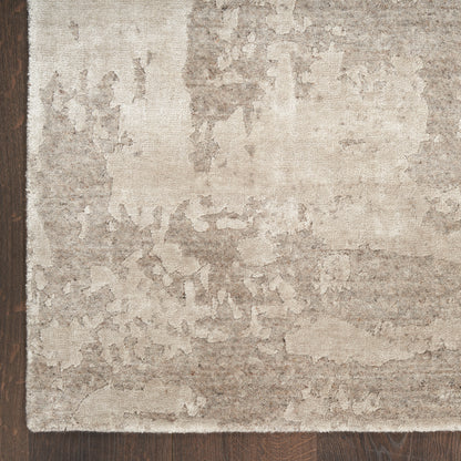 Soft beige distressed area rug with mottled taupe pattern on dark hardwood floor.