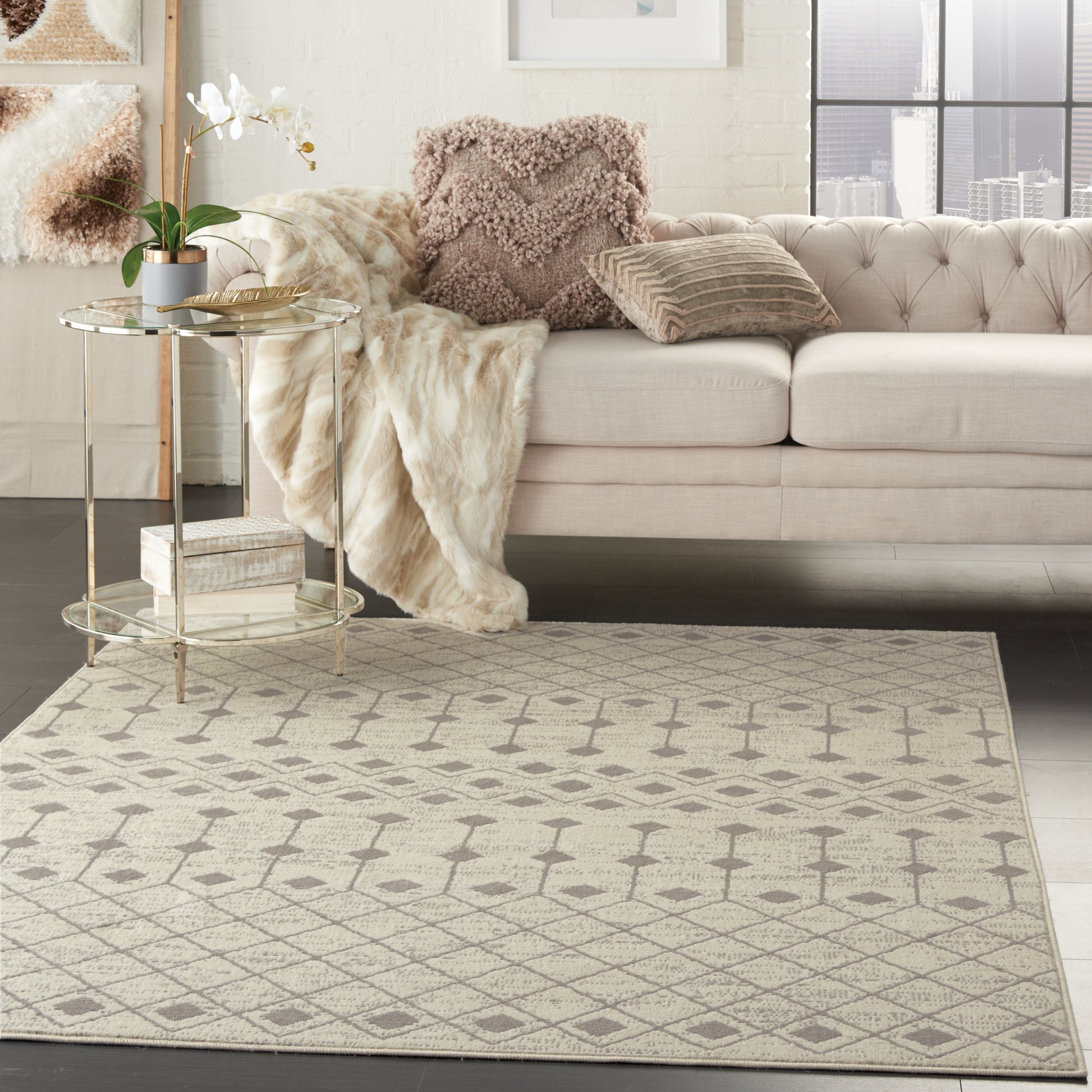 Neutral living room with tufted beige sofa, fluffy throw, geometric beige area rug, round glass side table, plant, city view.