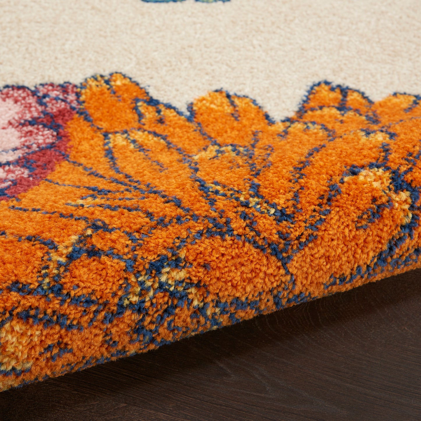 Close-up of a vibrant orange shag rug with blue accents and beige background on dark wood floor.