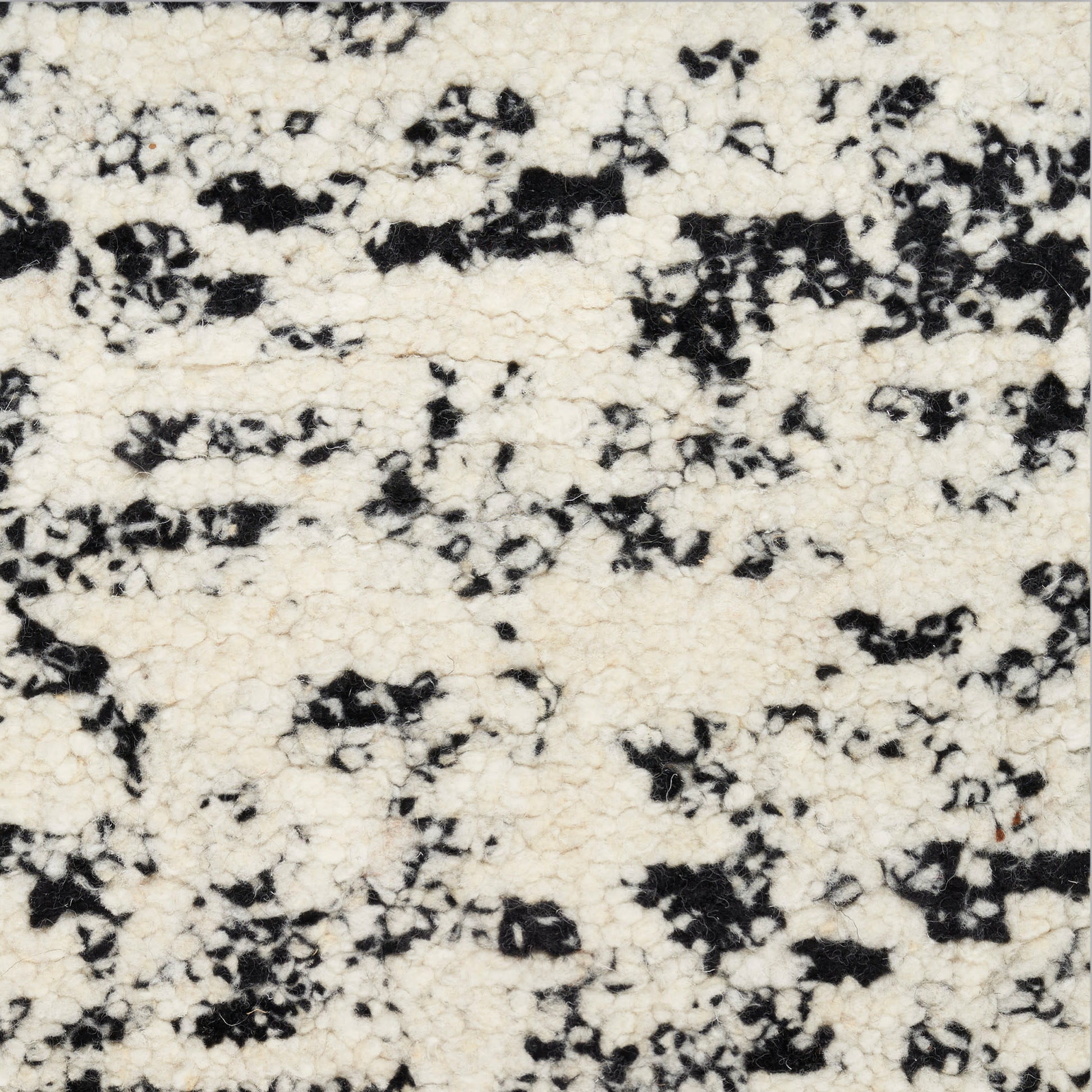 Cream boucle fabric with black irregular speckles; soft, textured textile for upholstery or garments.