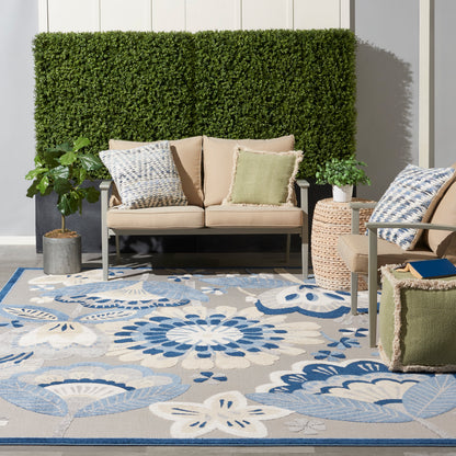 Outdoor seating area with beige cushioned sofa and chairs, blue floral rug, green accent pillows.