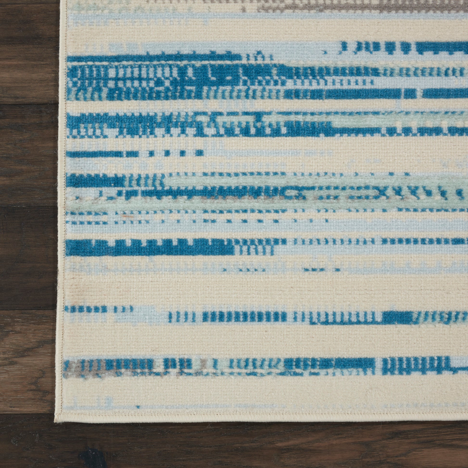 Rectangular area rug with cream base and blue brushstroke stripes on a dark wooden floor.