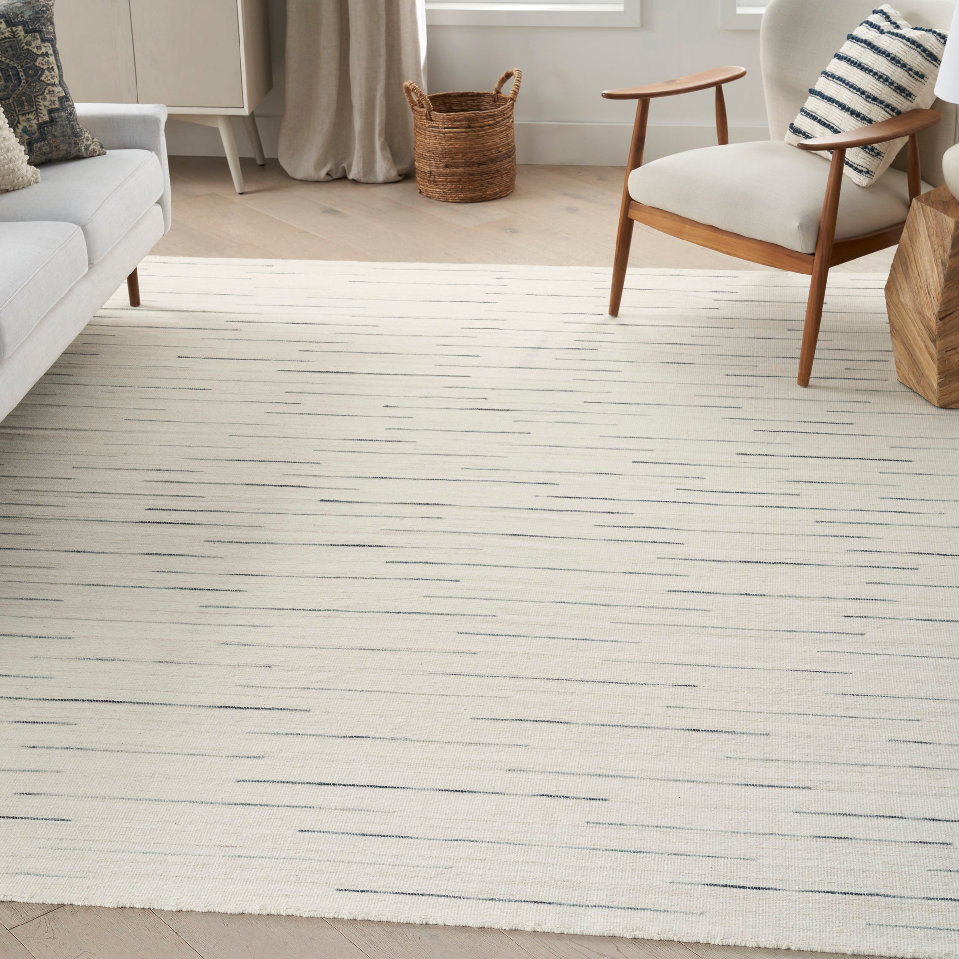 Cream area rug with thin gray stripes in a modern living room; light sofa, wooden chair, woven basket.
