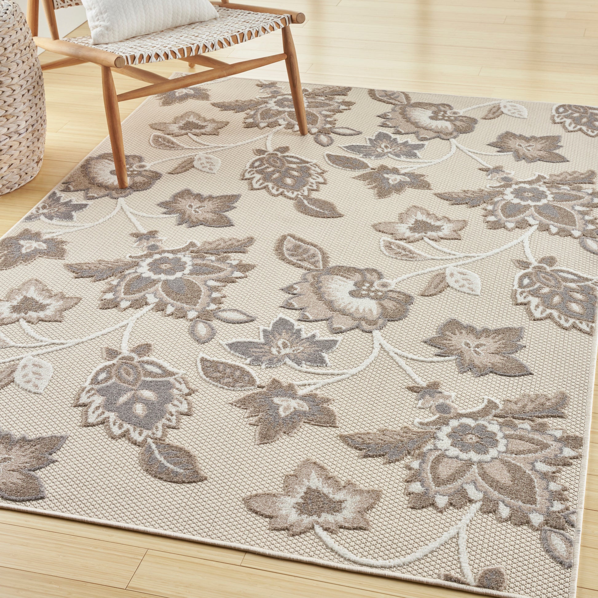 Beige floral area rug with taupe flowers and vines on a light dotted background in a cozy living space.