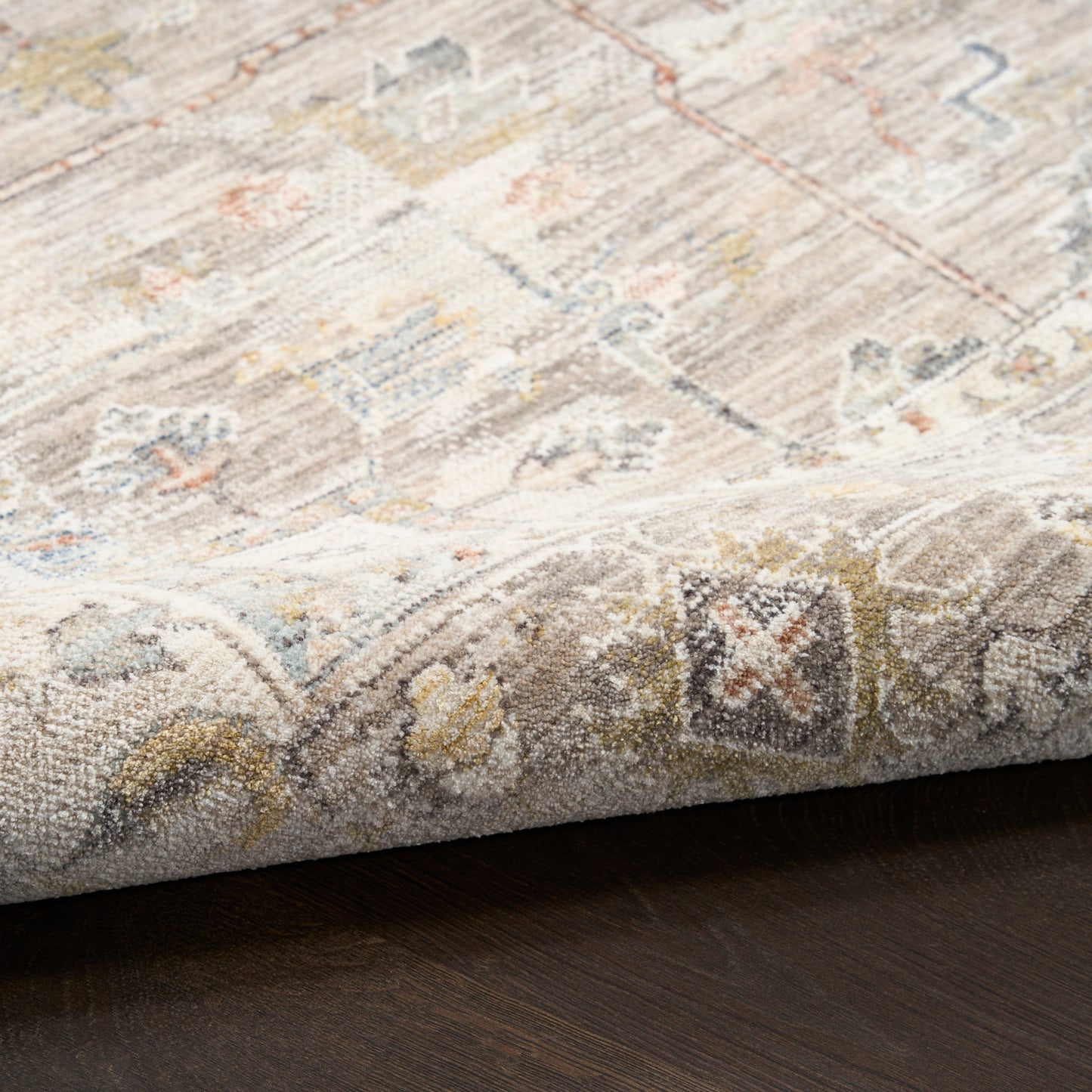 Rectangular beige woven rug with muted vintage oriental pattern in blues, yellows, grays; soft pile on dark wood floor.