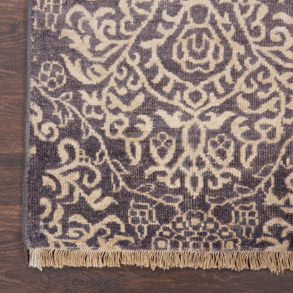 Purple & cream damask-patterned rug with fringe along the bottom edge on a wooden floor.
