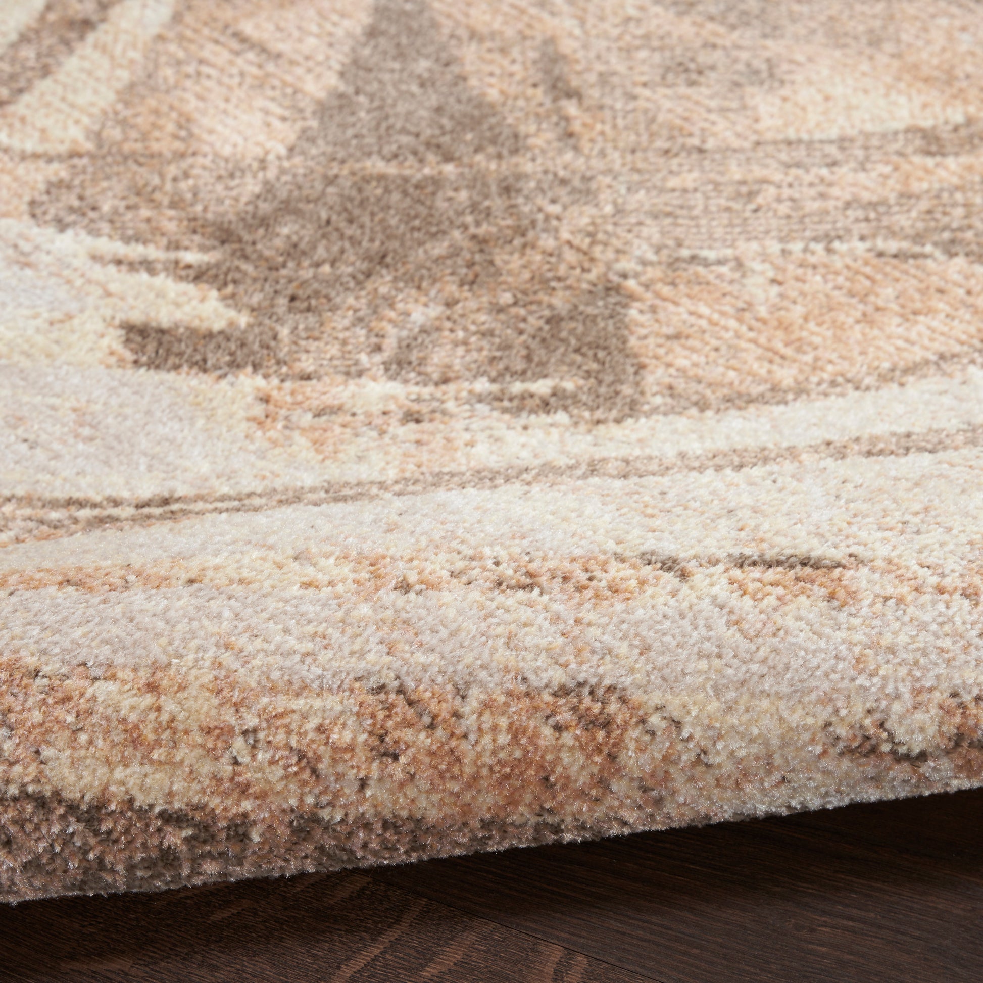Beige and tan patterned area rug with plush pile and folded edge on a dark wooden floor.