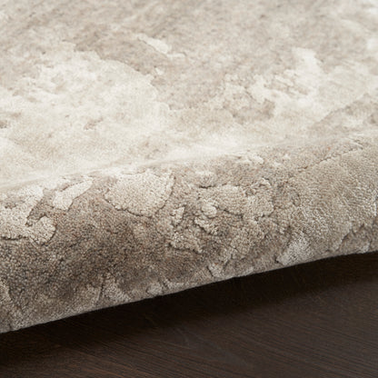 Soft plush beige rug with subtle mottled pattern, edge curled on dark wood floor.