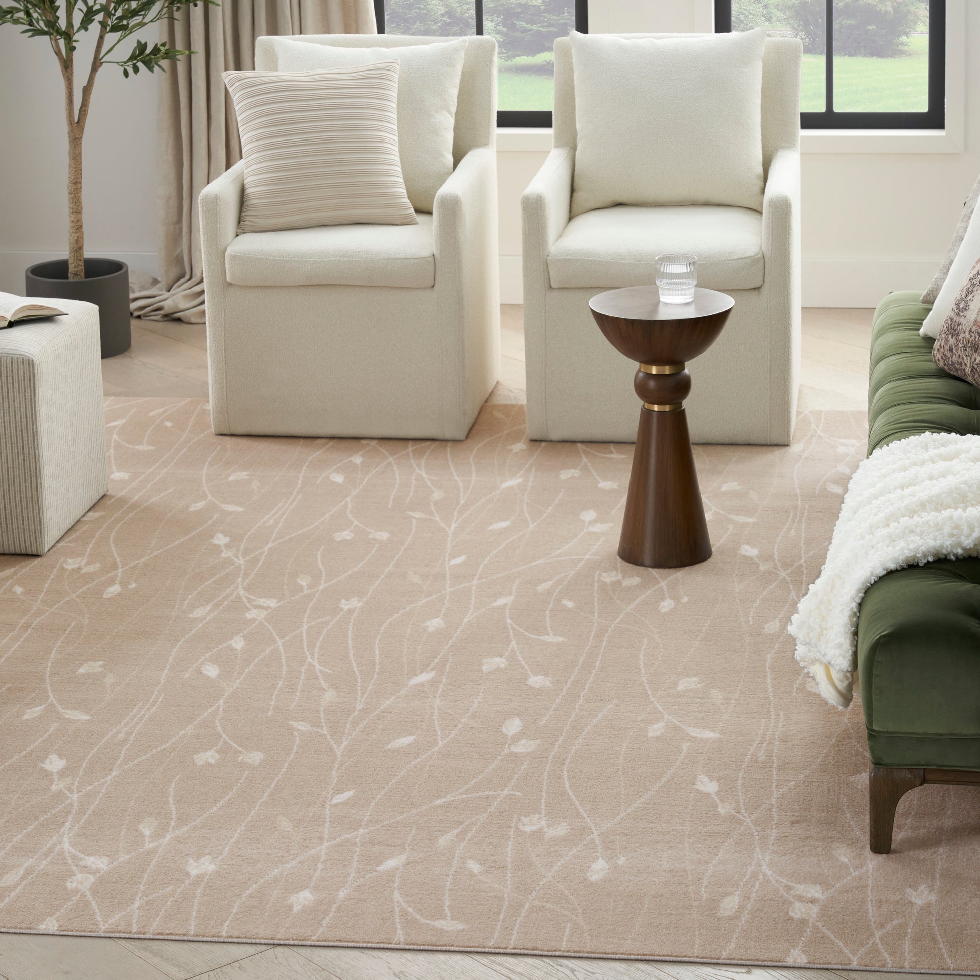 Beige area rug with white vine pattern in a bright living room with cream armchairs, wooden side table, and a green sofa.