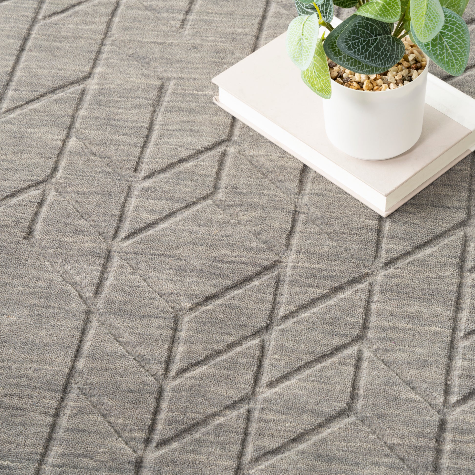 Grey geometric rug with diamond pattern & a white ceramic plant pot on a rectangular white tray.