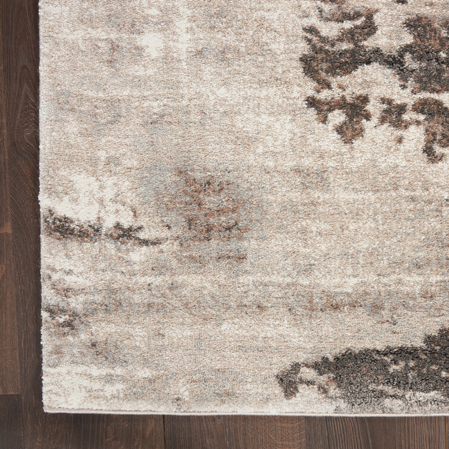 Rectangular beige abstract area rug with charcoal and gray patches on dark wood floor, modern neutral style.