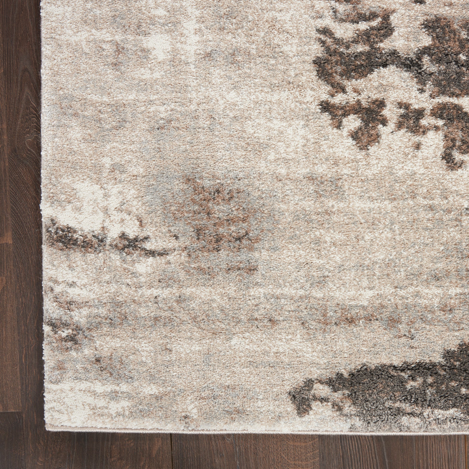 Rectangular beige abstract area rug with charcoal and gray patches on dark wood floor, modern neutral style.