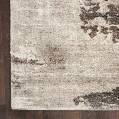 Rectangular beige abstract area rug with charcoal and gray patches on dark wood floor, modern neutral style.