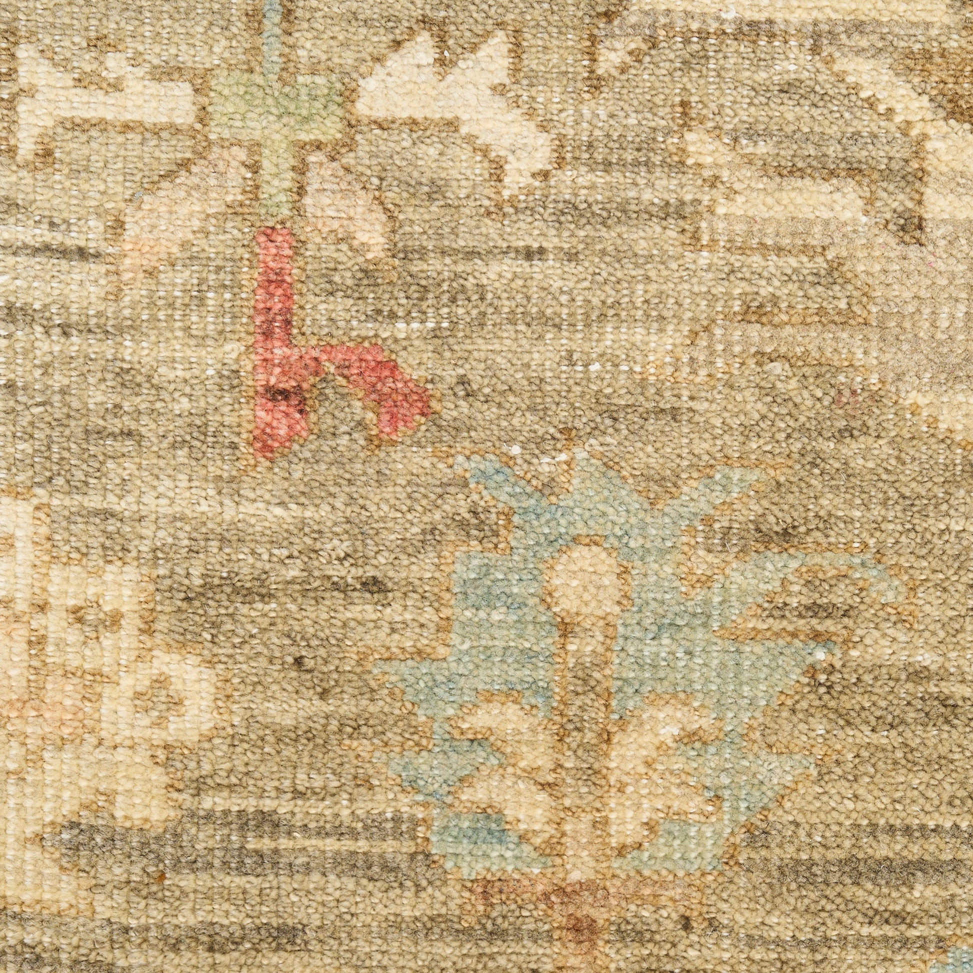 Close-up of a beige oriental rug with muted floral motifs in blue-green and red accents, woven pile texture.