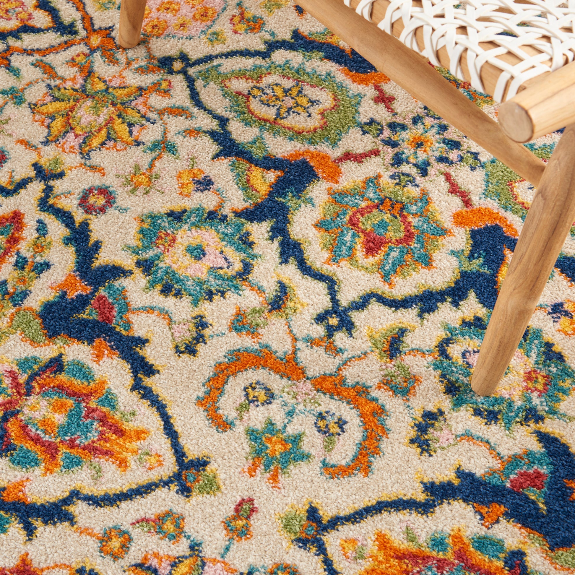 Colorful oriental-style area rug with a beige field and floral motifs in blue, orange, and green; textured pile near a wooden chair.