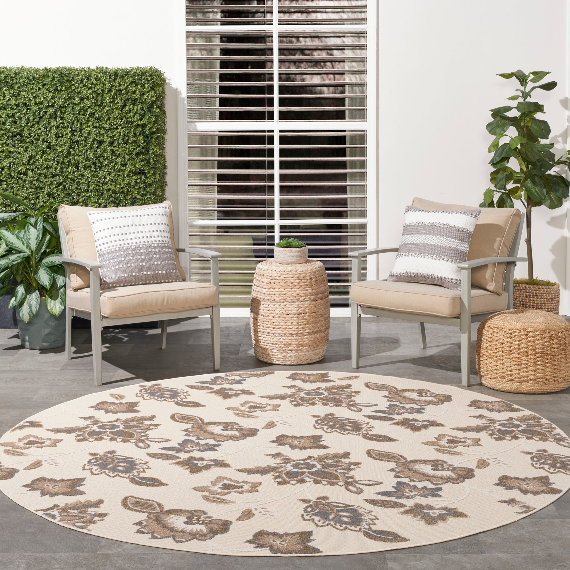 Outdoor patio with beige cushioned chairs around a round cream rug with brown floral pattern and a wicker side table.