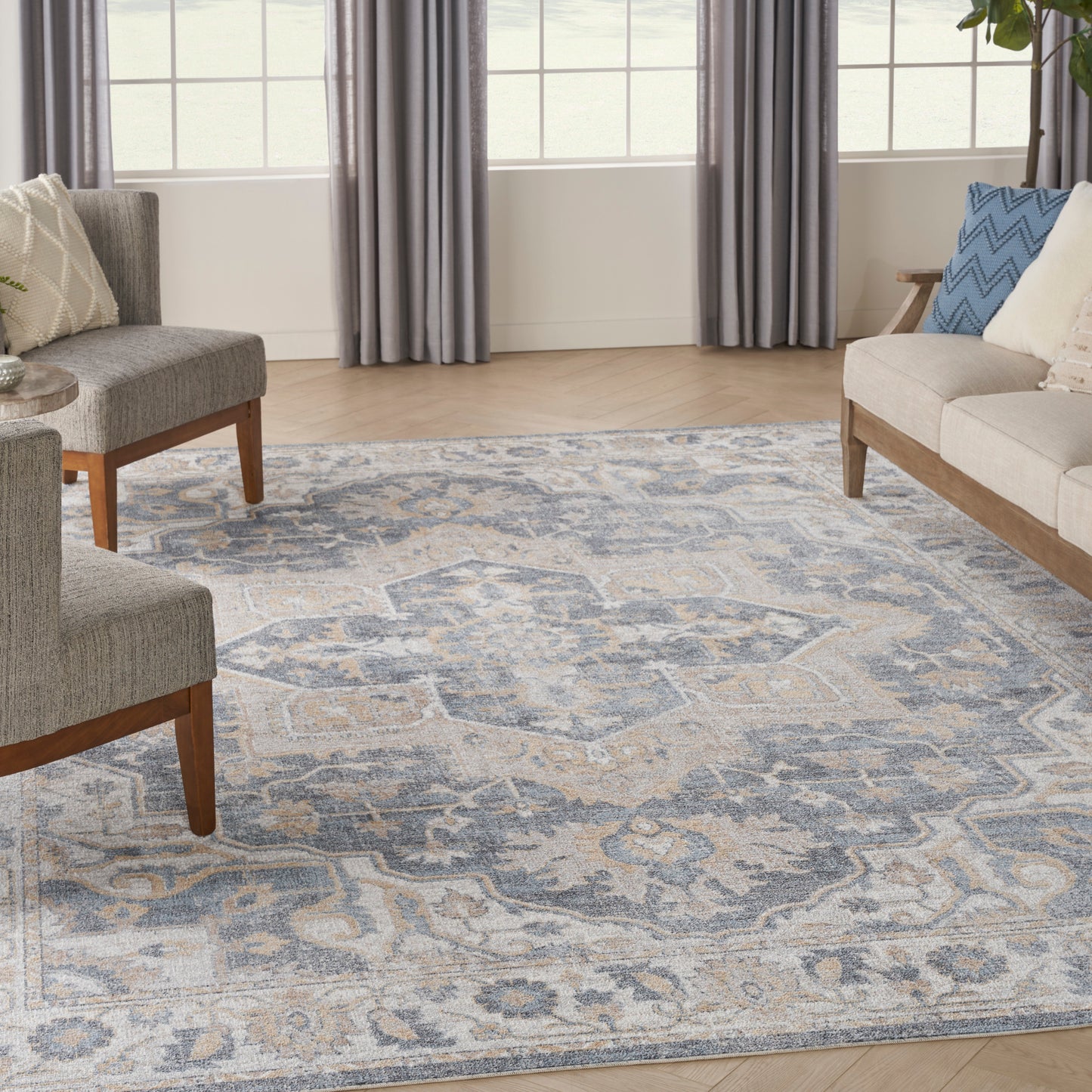 Blue-gray patterned area rug in a modern living room with gray upholstered chairs & beige sofa, wooden legs.