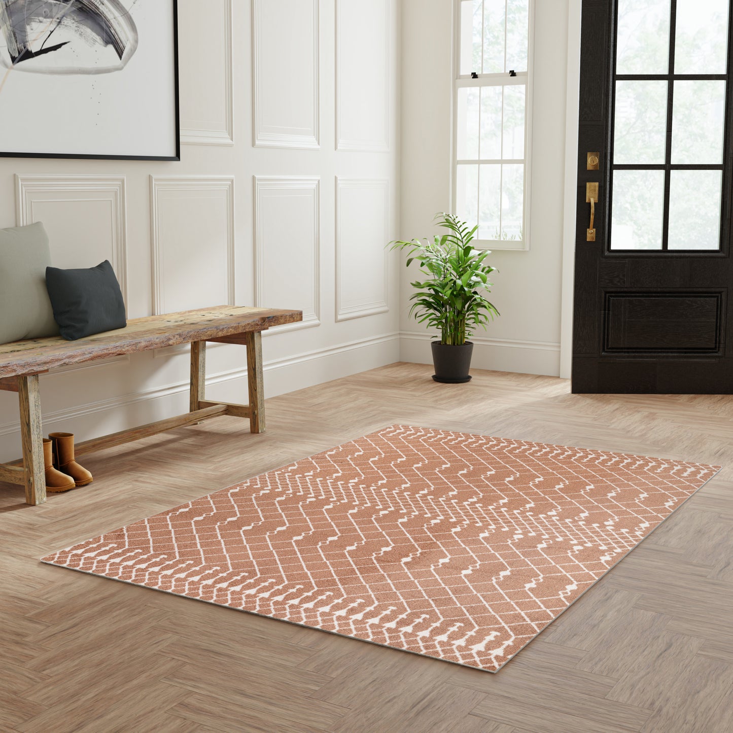 Peach chevron rug in entryway & wooden bench, framed art, potted plant, white paneled walls & dark front door.