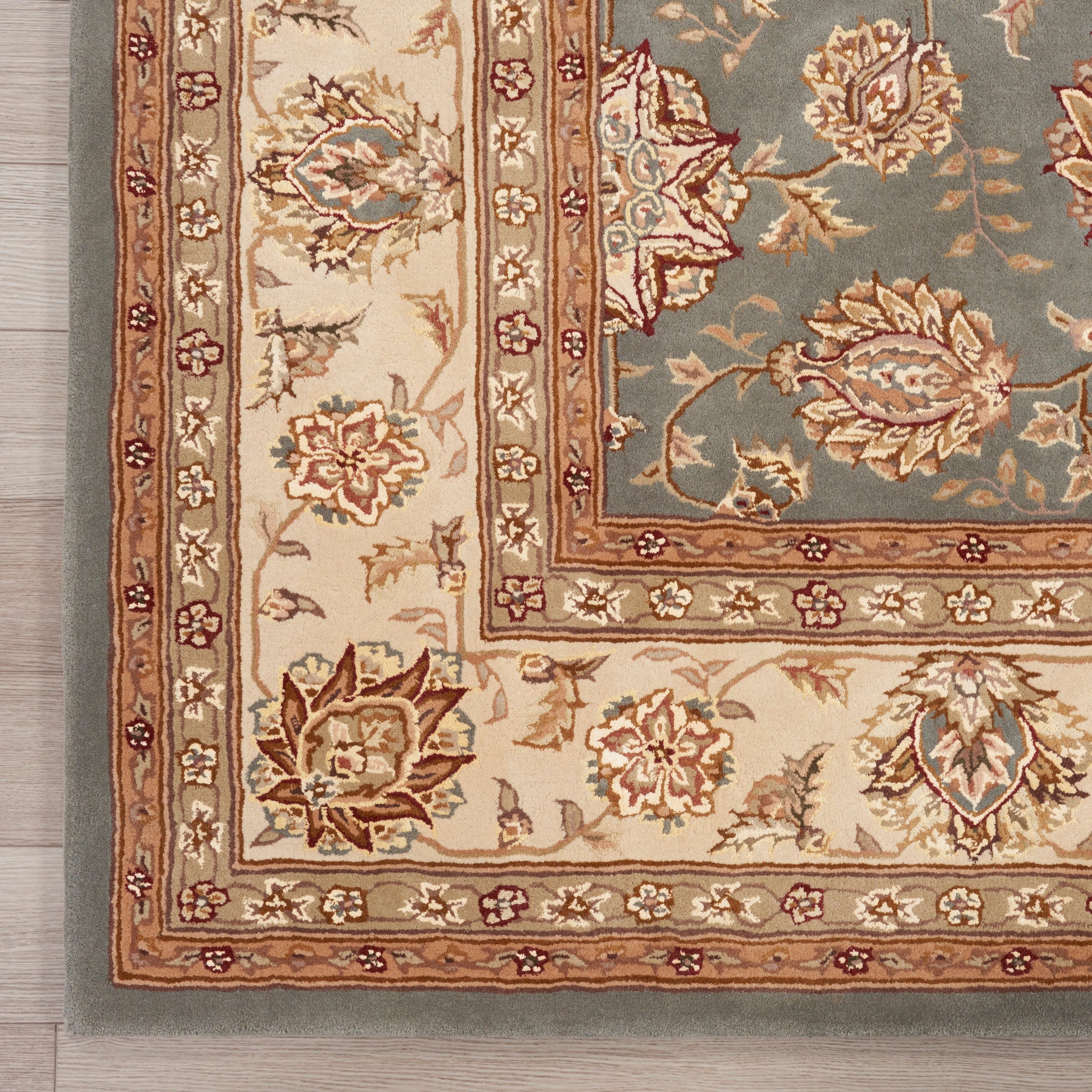 Corner of traditional oriental rug with ivory border, floral motifs in rust and brown, blue-green inner field.