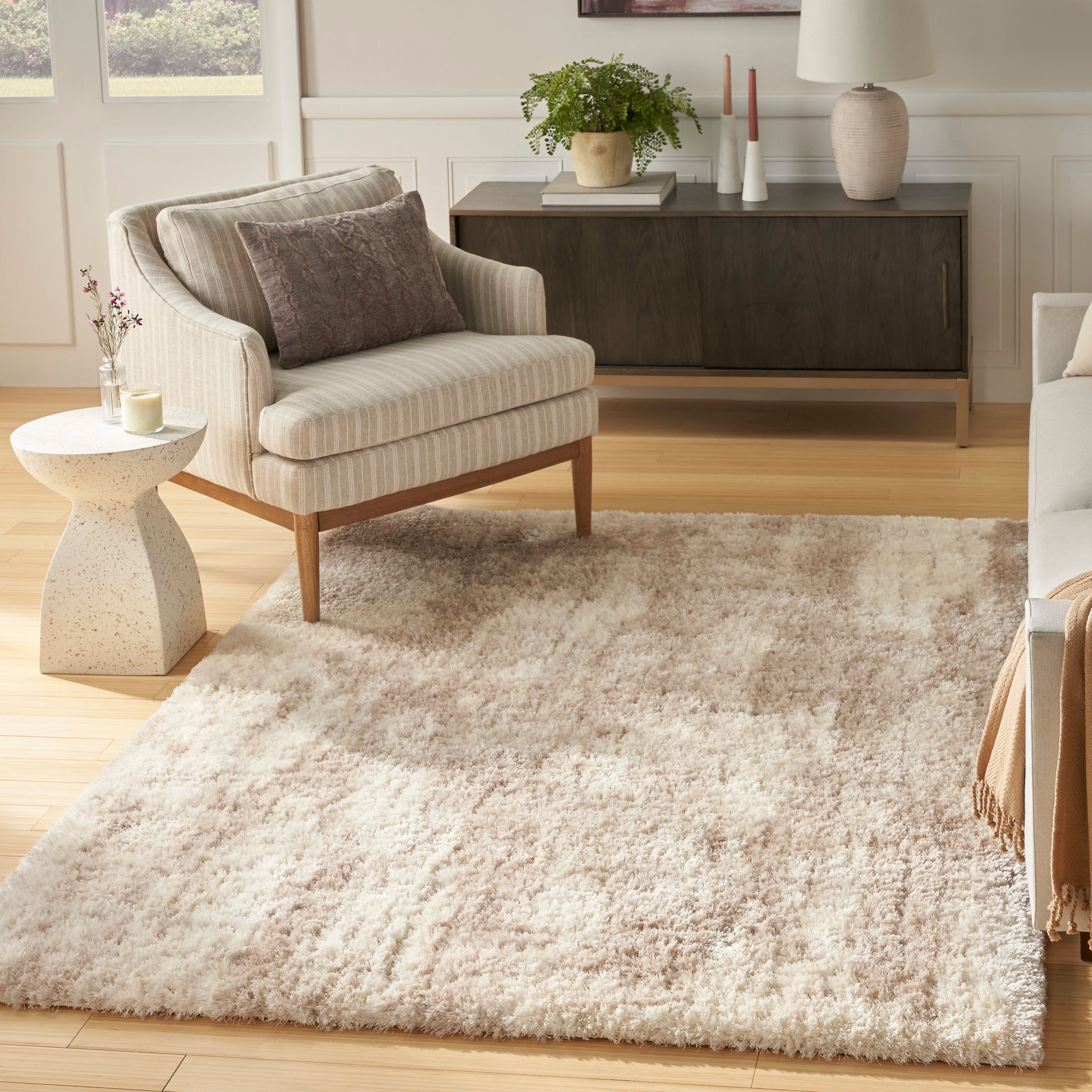 Cream shag area rug on light wood floor with beige striped armchair and dark wood console.