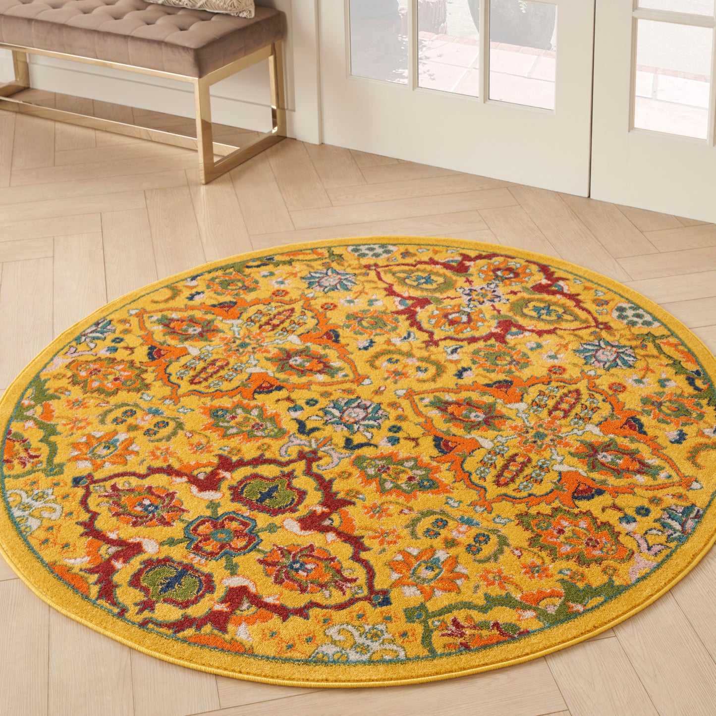 Round yellow rug with vibrant multicolor floral pattern on light wood floor near glass doors.