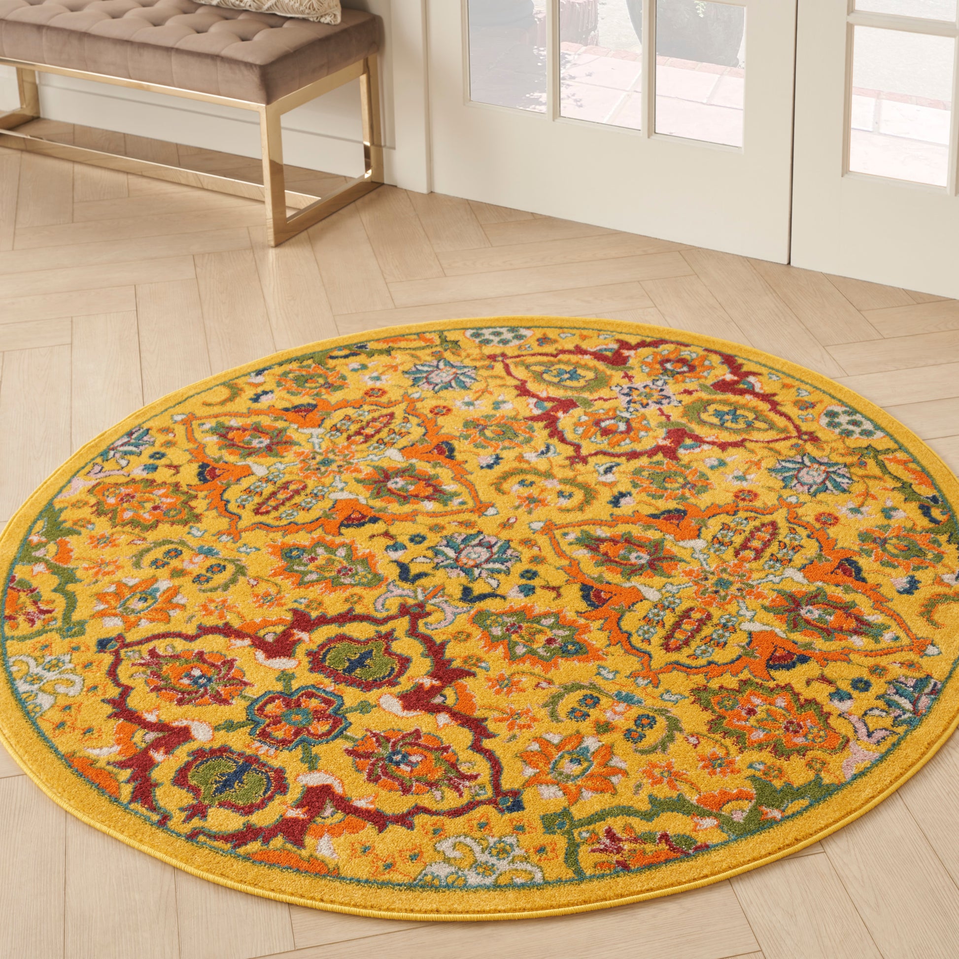 Round yellow rug with vibrant multicolor floral pattern on light wood floor near glass doors.