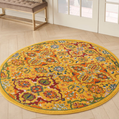 Round yellow rug with vibrant multicolor floral pattern on light wood floor near glass doors.