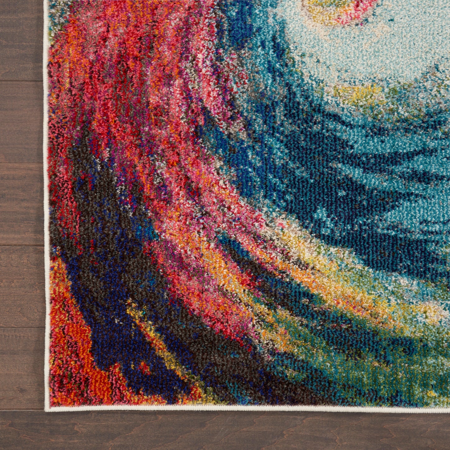 Colorful abstract rug with swirling red, pink, blue, teal & yellow patterns on a wooden floor.
