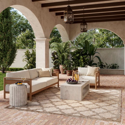 Outdoor patio rug on brick floor, 9' x 12', with cushioned wooden-frame sofas, a concrete coffee table, potted plants, arches and lanterns.