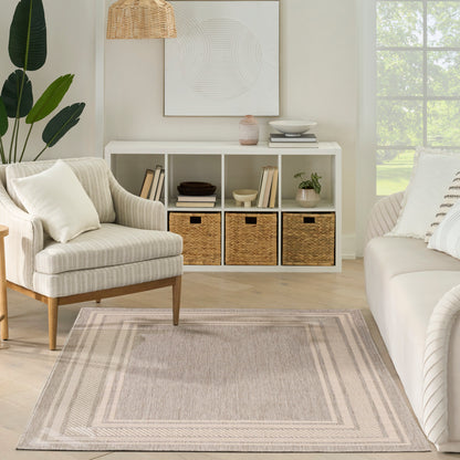Bright neutral living room with a cream striped armchair, white cubby shelf, wicker baskets, beige bordered rug, and a potted plant.