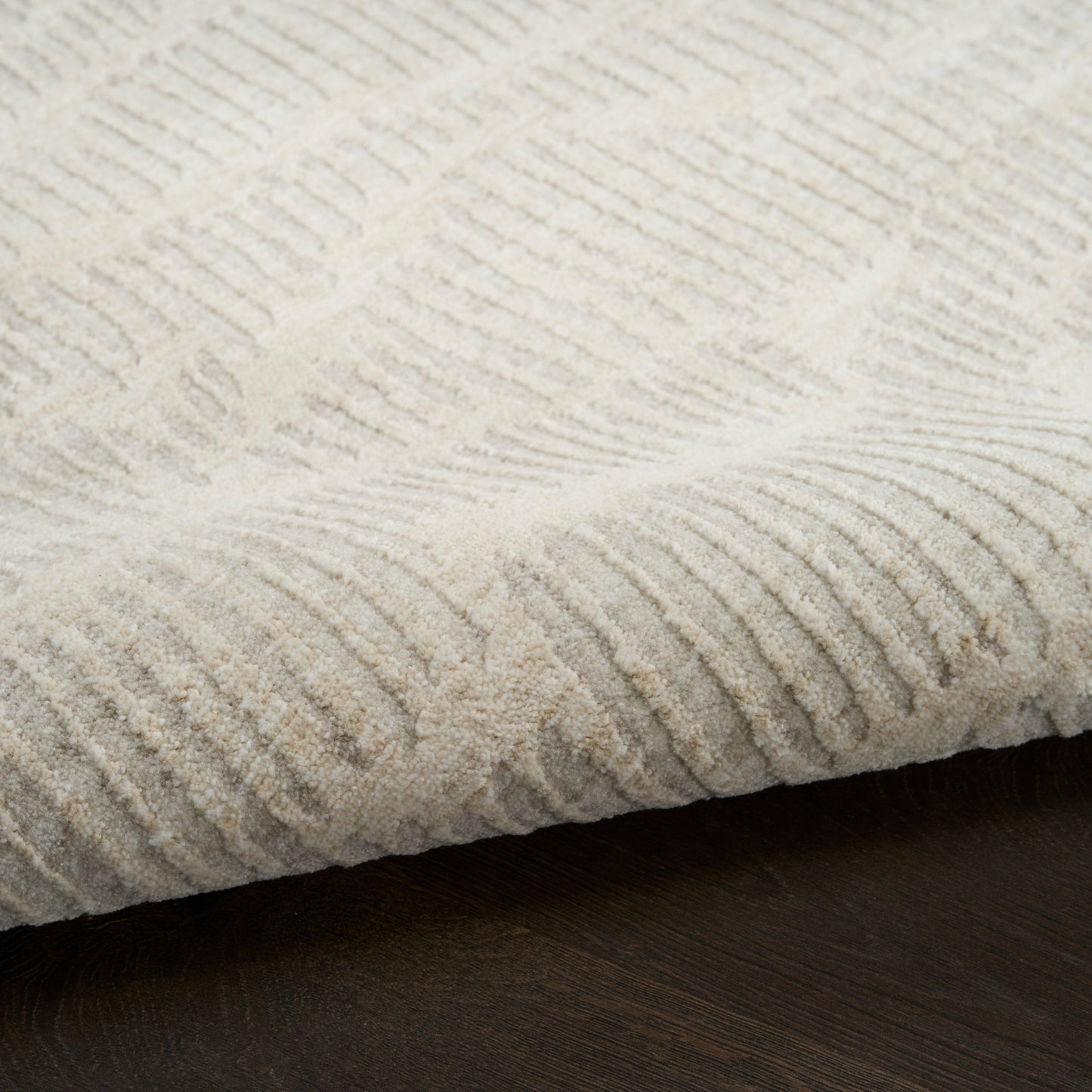Cream textured area rug with raised linear rib pattern, soft pile on dark wood floor.
