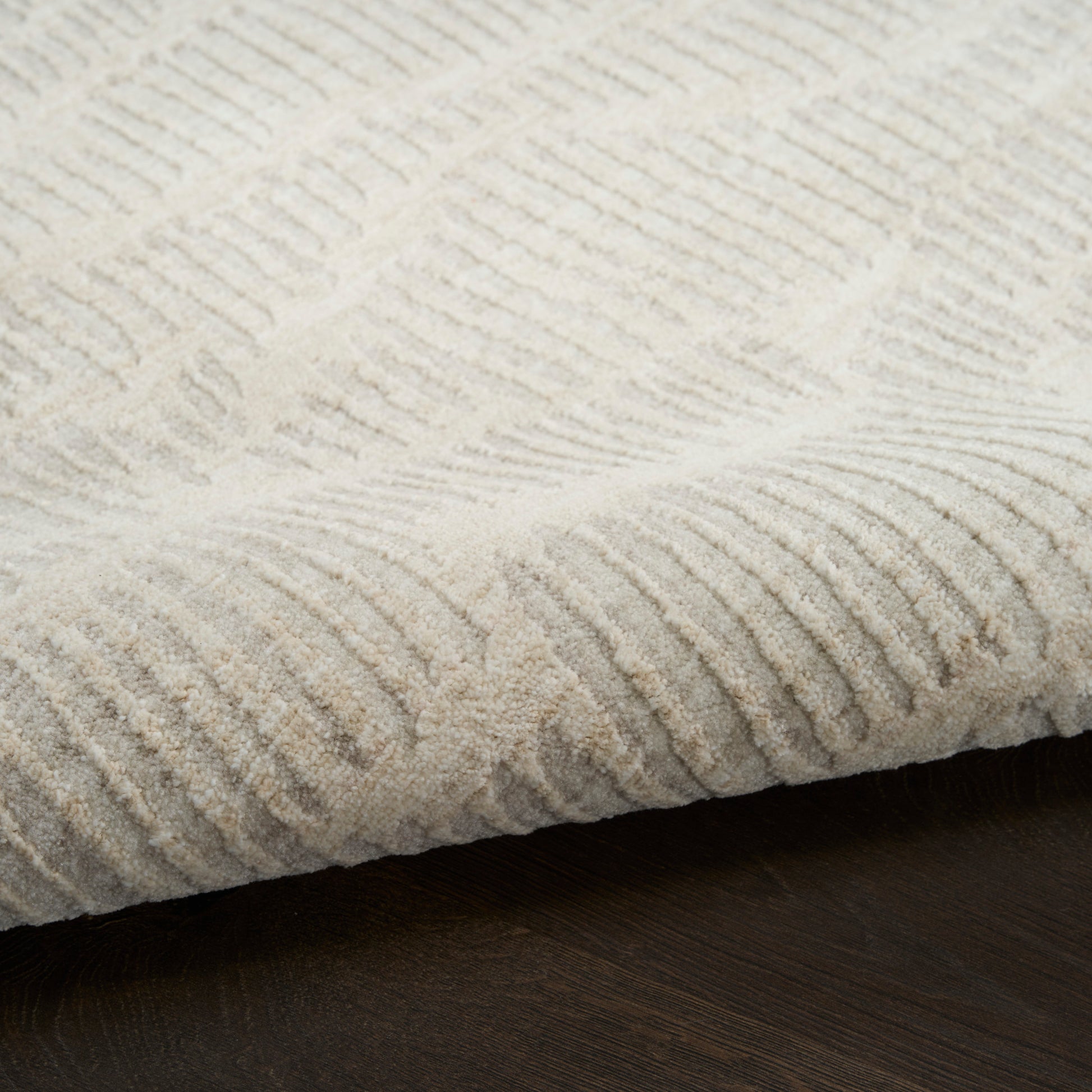 Cream textured area rug with raised linear rib pattern, soft pile on dark wood floor.