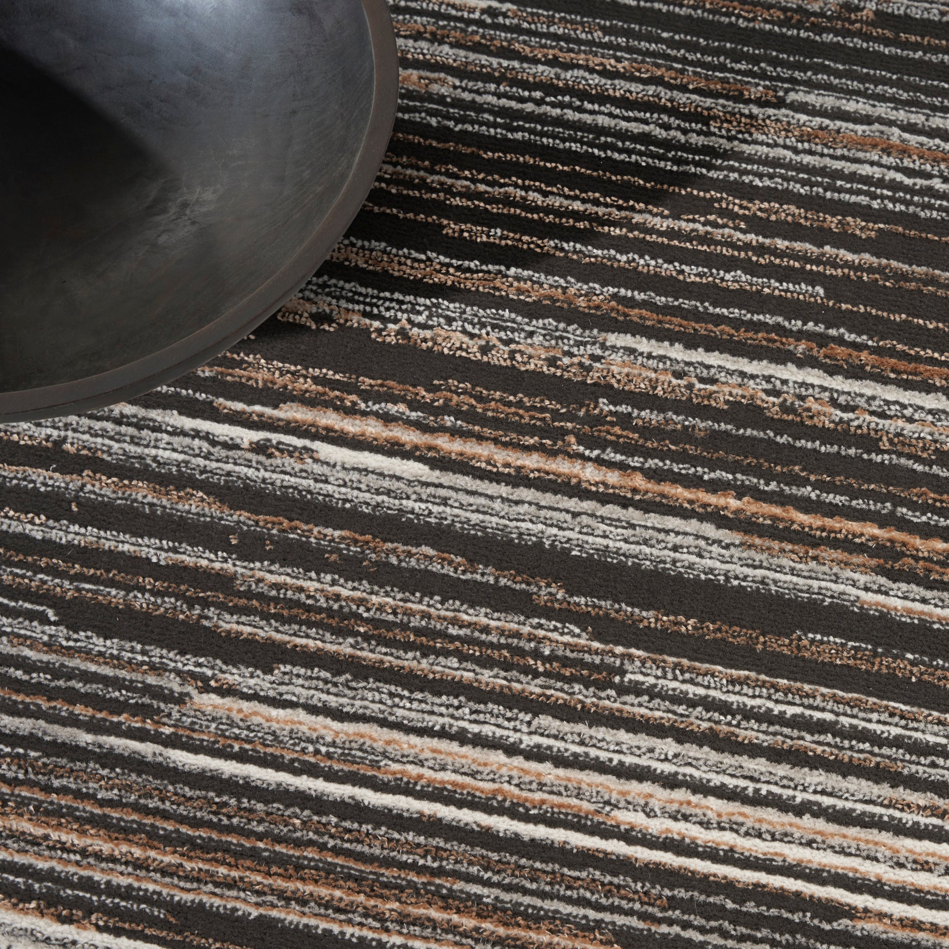 Dark round metal pan resting on a striped black, white & tan area rug; modern industrial decor