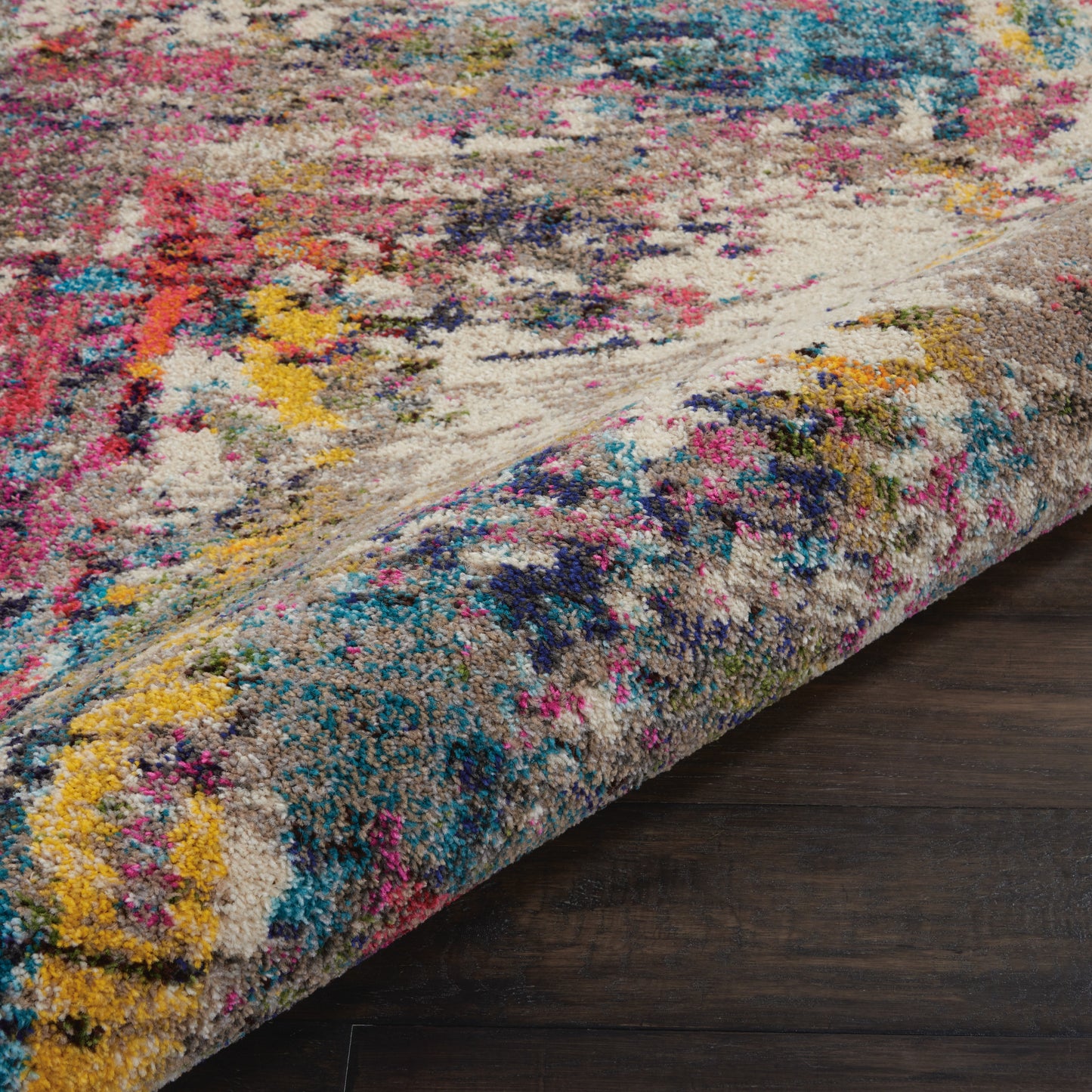 Plush, abstract multicolor area rug with beige base & pink, blue, yellow, teal accents; rolled edge reveals thick pile.