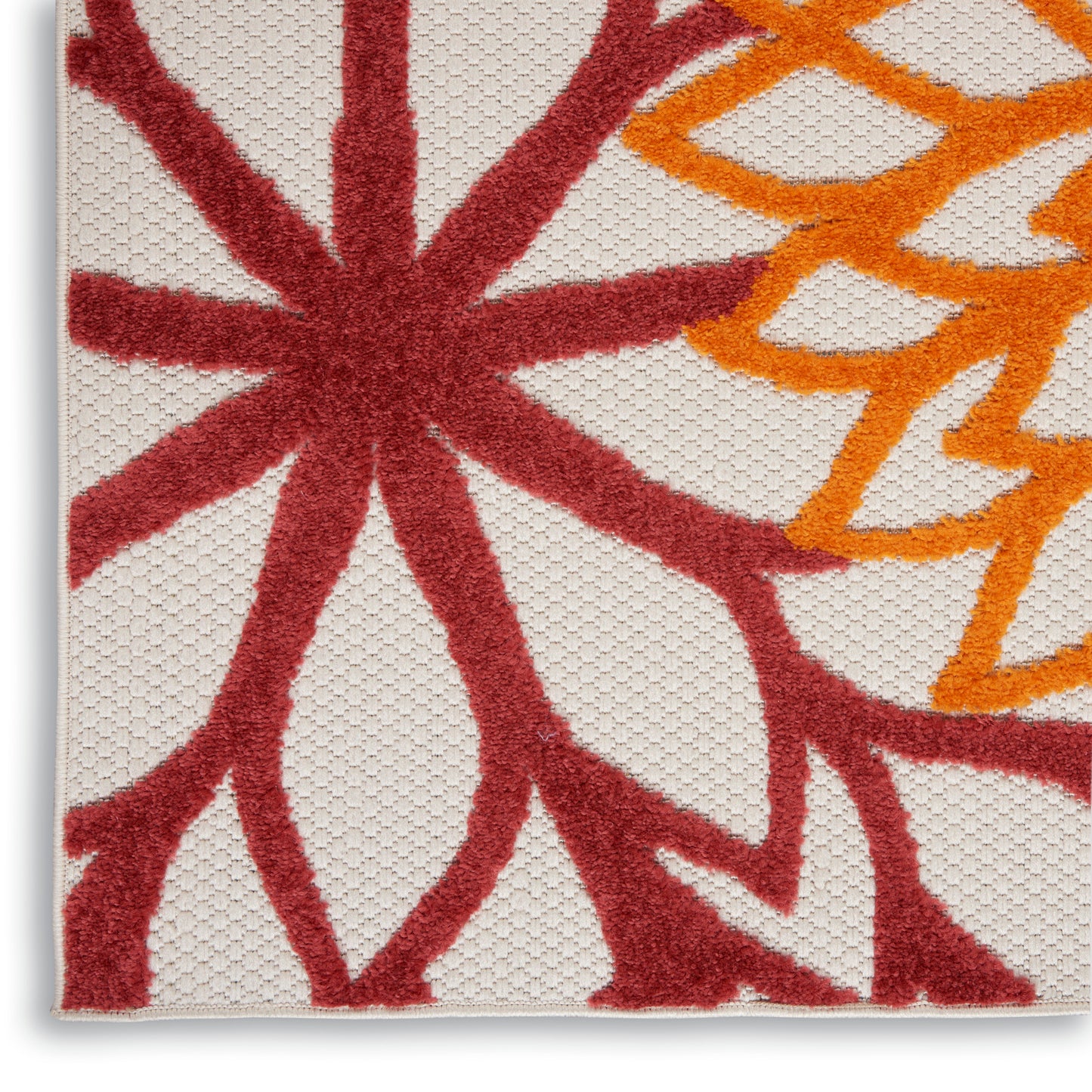 Beige woven rug close-up with large red starburst flower and orange curved lines, textured fibers.