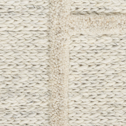 Cream rug close-up with cable-like texture and raised seam, cozy and soft.