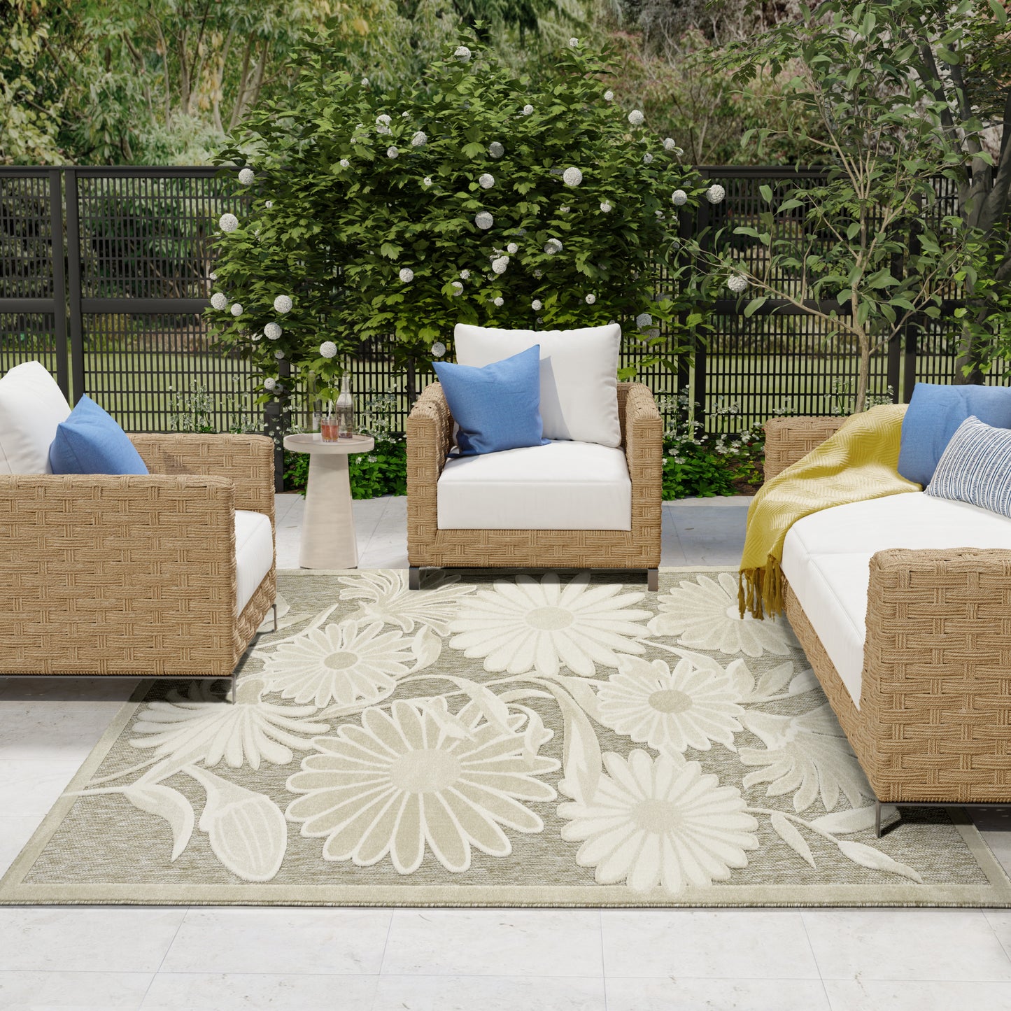 Outdoor beige floral rug on a patio with wicker seating, white cushions and blue pillows, and a round side table.