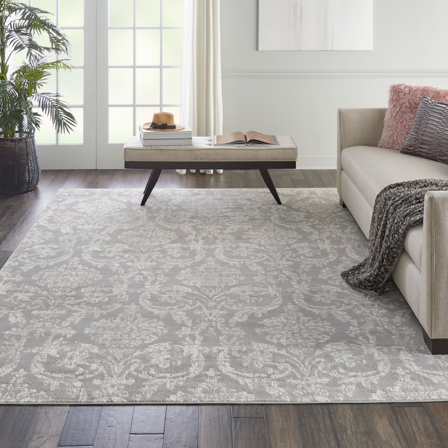 Light gray patterned area rug, 7' x 10', in a modern living room with a beige sofa, throw blanket, coffee table, and a potted plant.