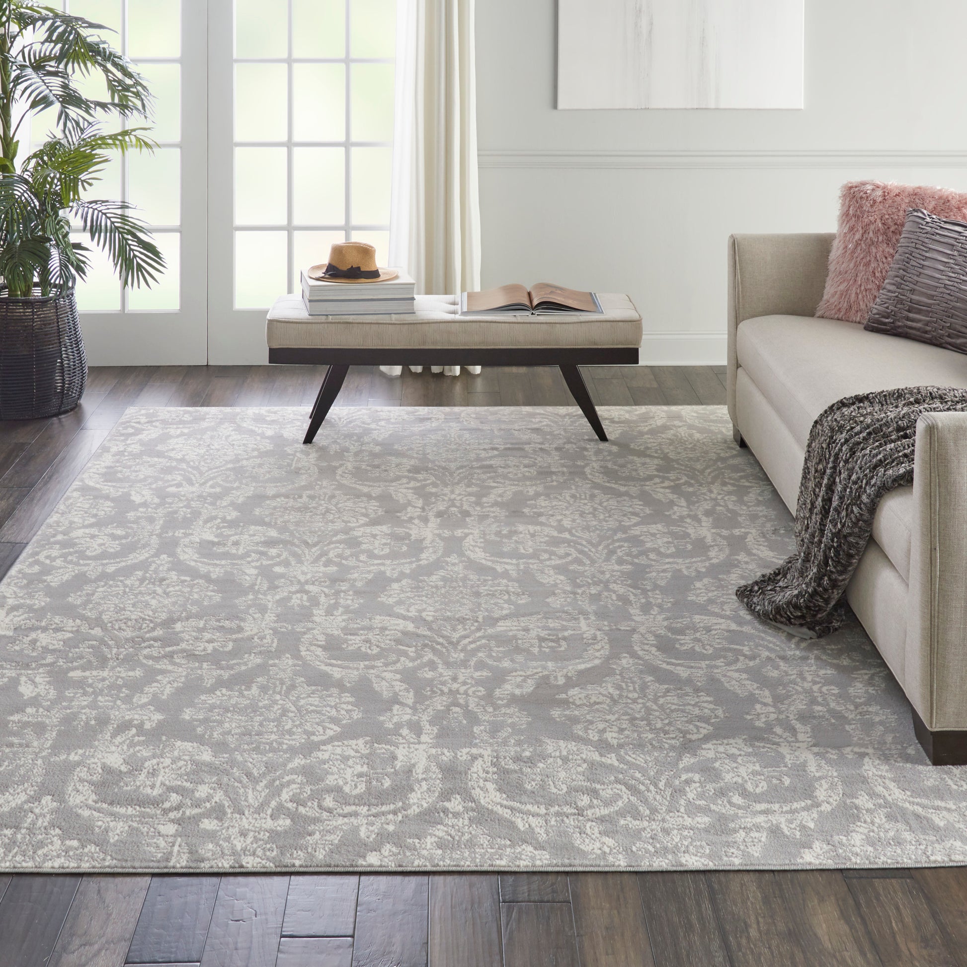 Light gray patterned area rug, 7' x 10', in a modern living room with a beige sofa, throw blanket, coffee table, and a potted plant.